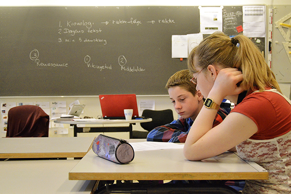 2 teenagere ved skolebord kigger på en opgave i fællesskab